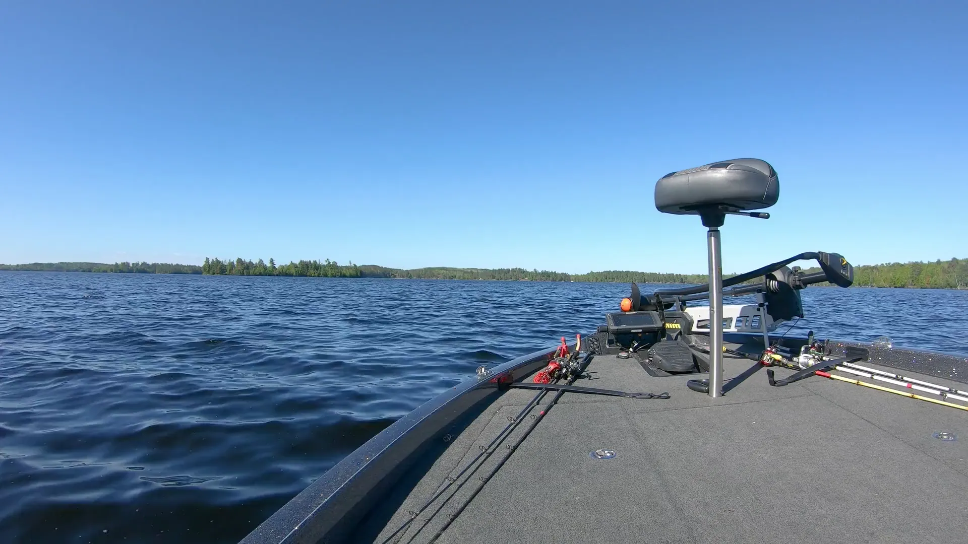 Bow of a bass boat on a lake with its trolling motor, pedestal seat and fishfinder